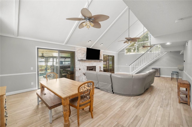 dining room featuring ceiling fan, a stone fireplace, light hardwood / wood-style flooring, and high vaulted ceiling