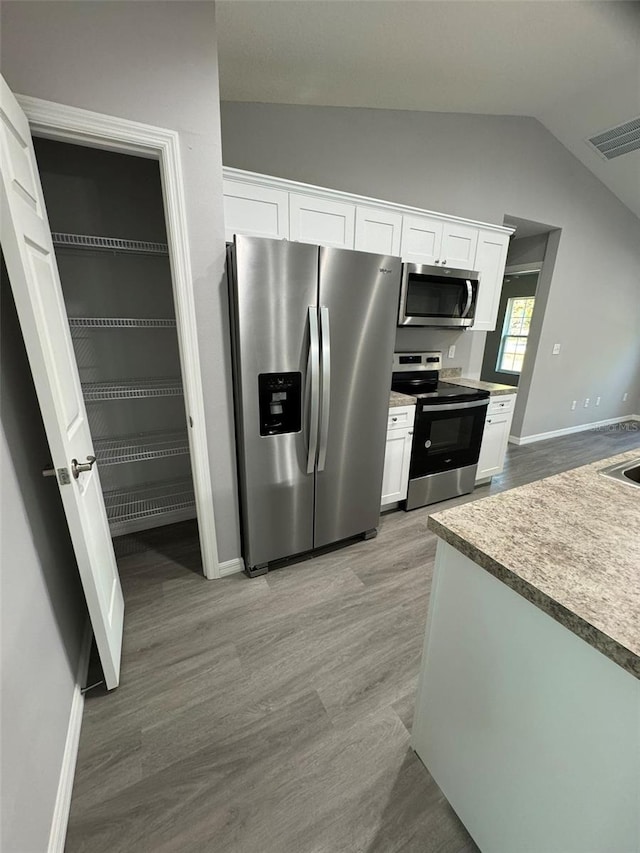 kitchen featuring white cabinetry, light wood-type flooring, vaulted ceiling, and appliances with stainless steel finishes