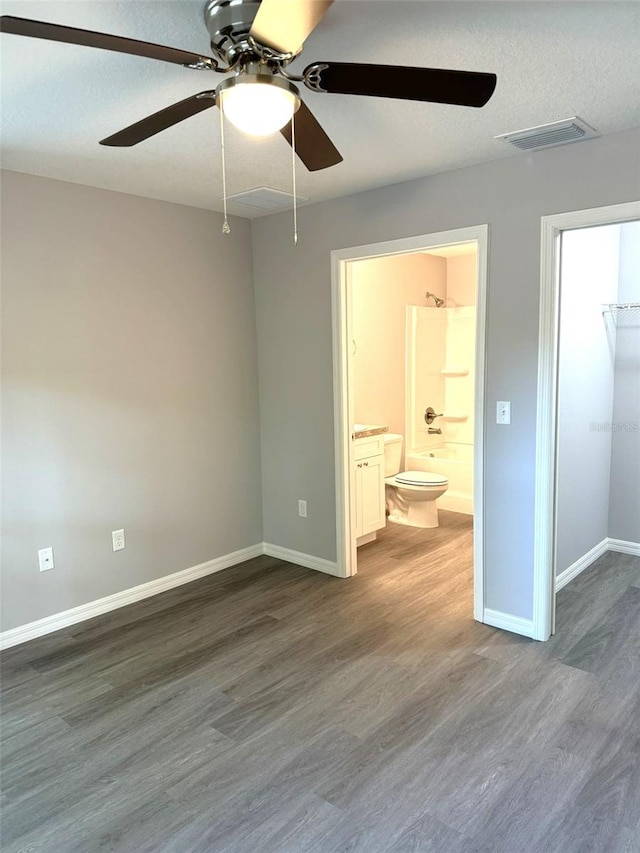 unfurnished bedroom with ceiling fan, hardwood / wood-style floors, connected bathroom, a textured ceiling, and a spacious closet