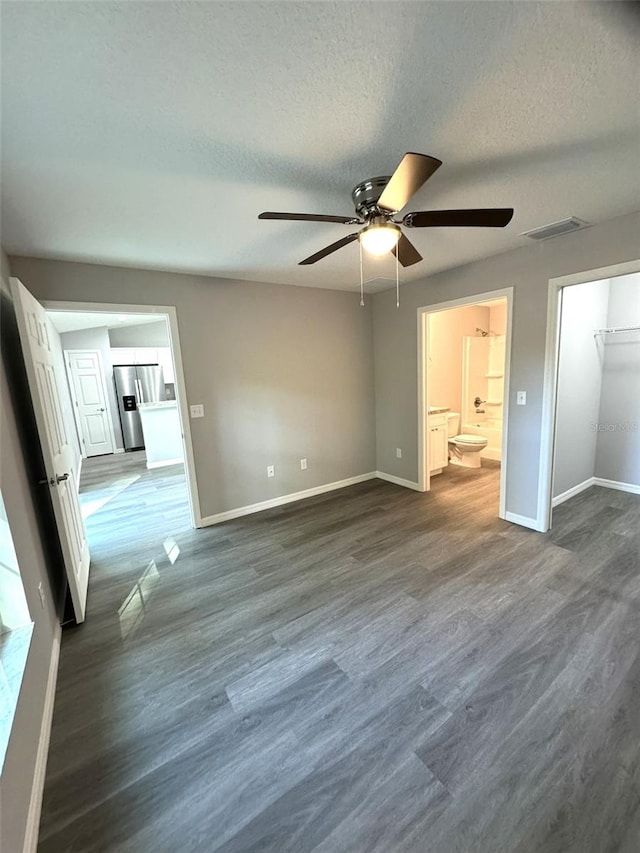 unfurnished bedroom featuring connected bathroom, dark wood-type flooring, a textured ceiling, and stainless steel refrigerator with ice dispenser