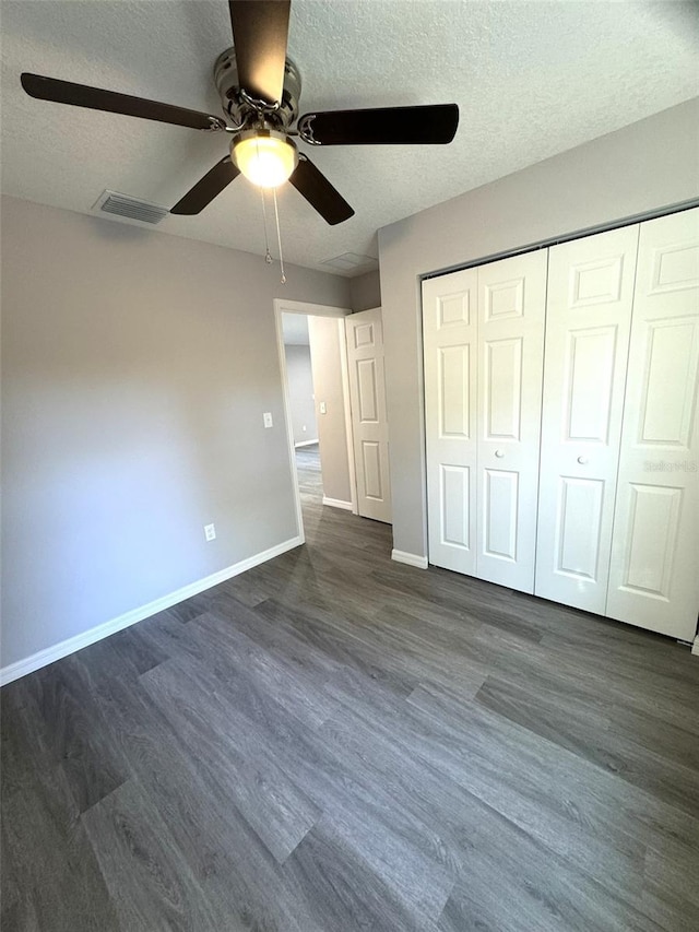 unfurnished bedroom with ceiling fan, dark wood-type flooring, a textured ceiling, and a closet