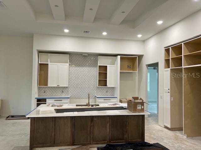 kitchen featuring an island with sink, sink, white cabinetry, and tasteful backsplash