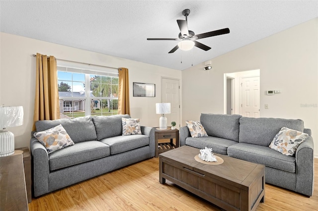 living room with ceiling fan, vaulted ceiling, a textured ceiling, and light hardwood / wood-style floors