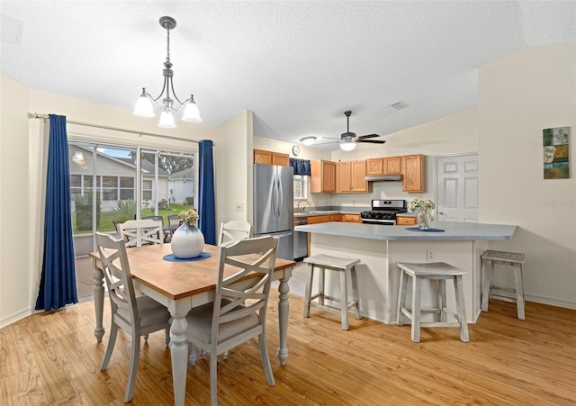 dining room with vaulted ceiling, sink, ceiling fan with notable chandelier, and light hardwood / wood-style flooring