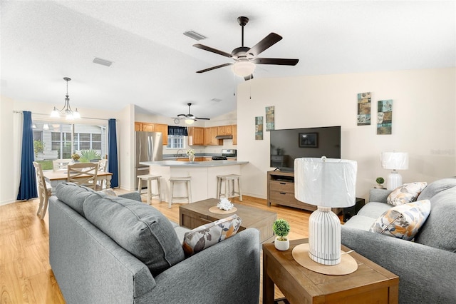 living room with vaulted ceiling, ceiling fan with notable chandelier, a textured ceiling, and light hardwood / wood-style flooring