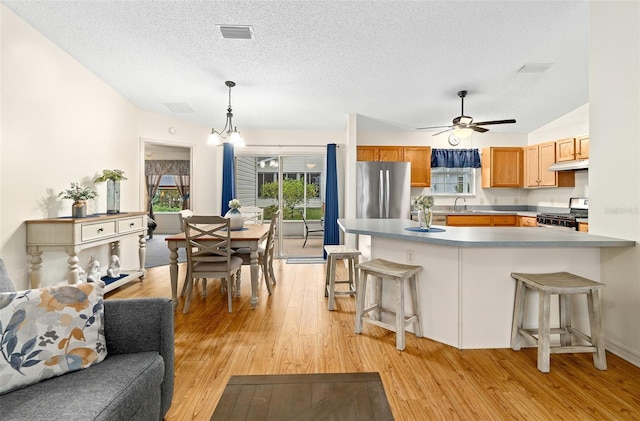 kitchen featuring a breakfast bar area, decorative light fixtures, light hardwood / wood-style flooring, a textured ceiling, and appliances with stainless steel finishes