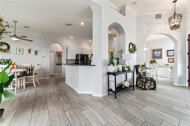 kitchen with black refrigerator, backsplash, ceiling fan with notable chandelier, white cabinets, and crown molding