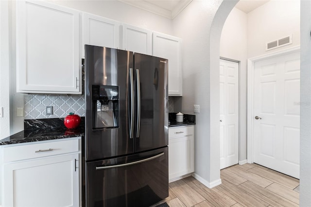 kitchen with white cabinets, dark stone counters, backsplash, and stainless steel fridge