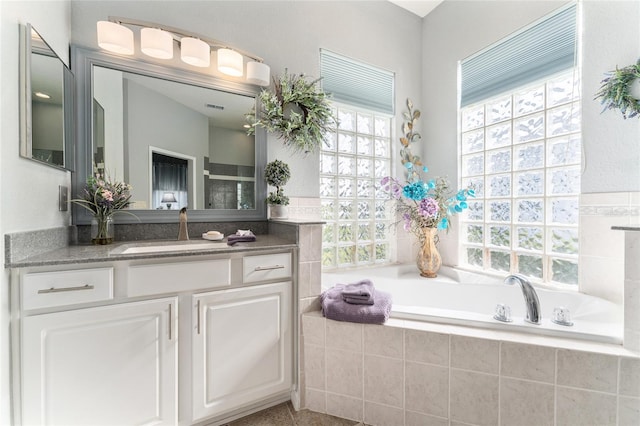 bathroom featuring a relaxing tiled bath, vanity, and a wealth of natural light