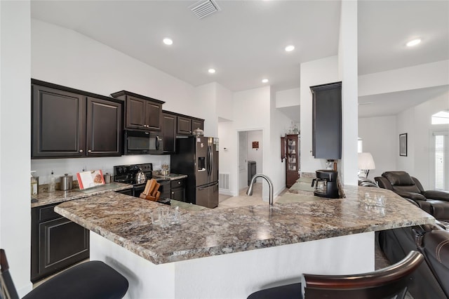 kitchen with black appliances, kitchen peninsula, stone countertops, and a breakfast bar area