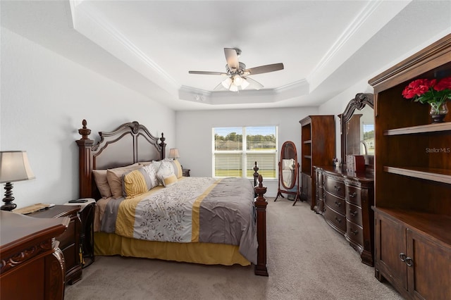 carpeted bedroom with a tray ceiling, ceiling fan, and crown molding