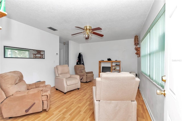 living room with a textured ceiling, ceiling fan, and light wood-type flooring