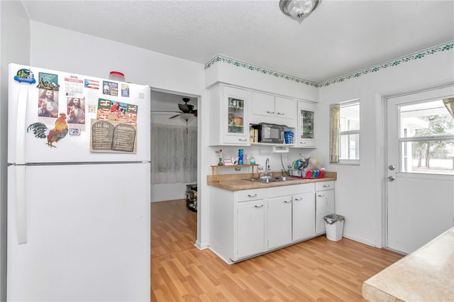 kitchen with white fridge, ceiling fan, white cabinets, light wood-type flooring, and sink