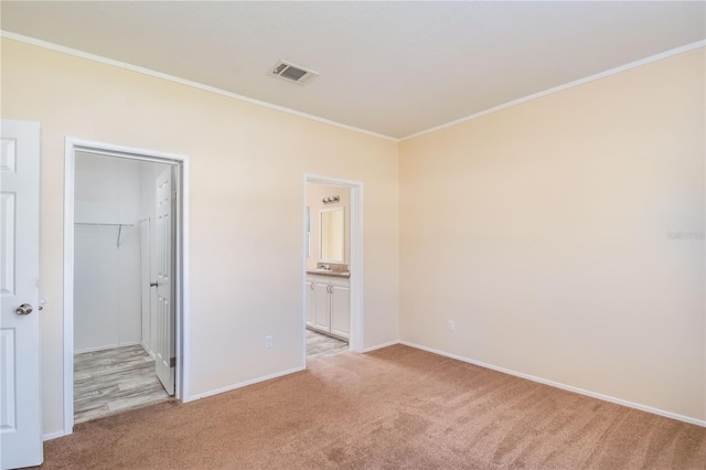 unfurnished bedroom with light carpet, a spacious closet, a closet, and crown molding