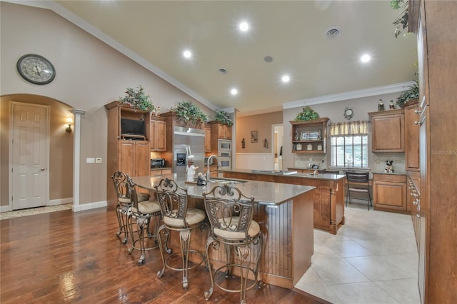 kitchen featuring crown molding, light hardwood / wood-style flooring, vaulted ceiling, appliances with stainless steel finishes, and a center island with sink