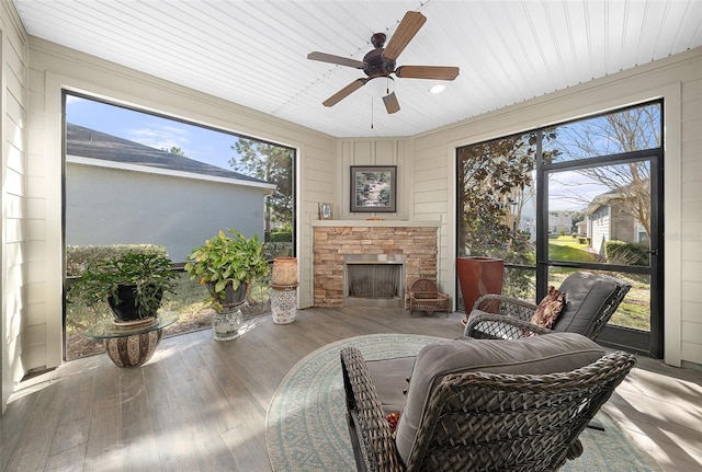 sunroom with a stone fireplace and ceiling fan