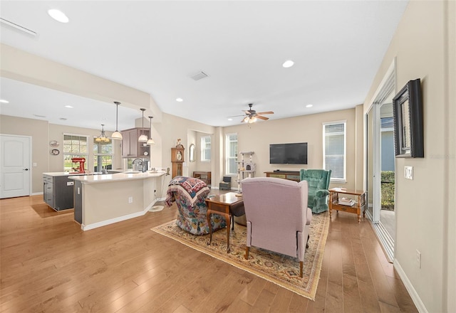 living room featuring ceiling fan with notable chandelier and light hardwood / wood-style flooring