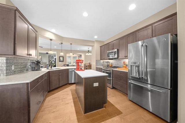 kitchen with kitchen peninsula, backsplash, appliances with stainless steel finishes, light wood-type flooring, and a kitchen island