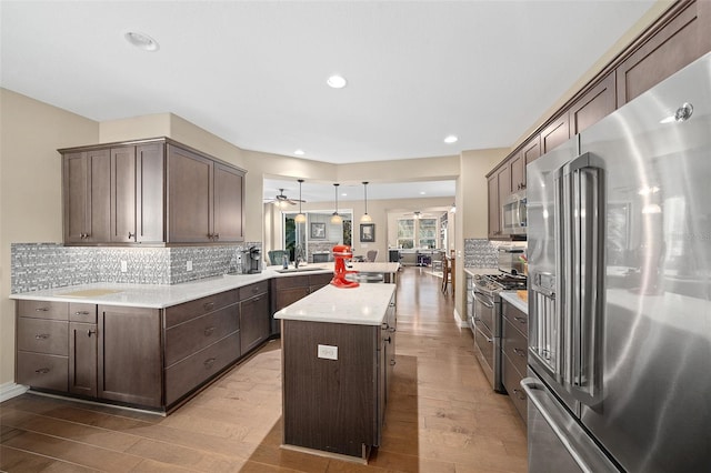 kitchen with backsplash, stainless steel appliances, decorative light fixtures, and light wood-type flooring