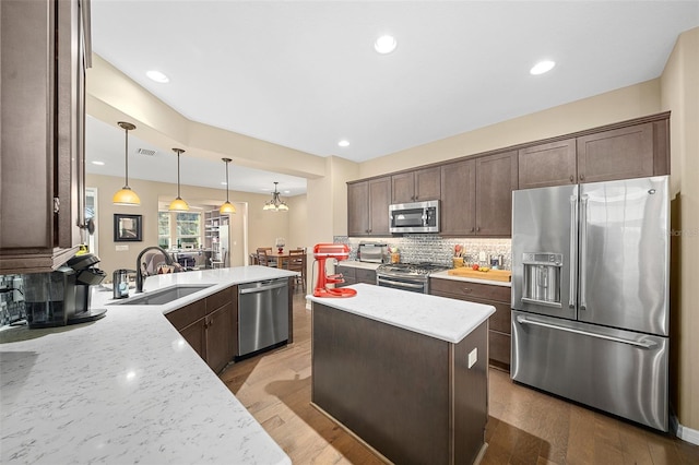 kitchen featuring sink, light hardwood / wood-style flooring, stainless steel appliances, tasteful backsplash, and decorative light fixtures