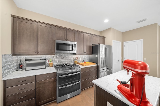 kitchen with light stone countertops, backsplash, light hardwood / wood-style flooring, stainless steel appliances, and dark brown cabinets