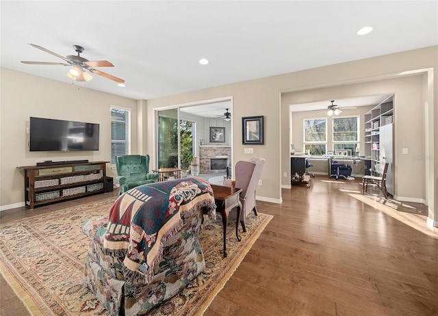 living room with light hardwood / wood-style floors, ceiling fan, and a stone fireplace