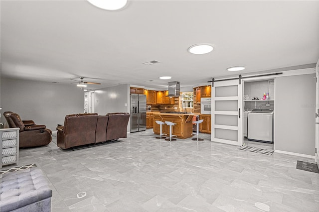 interior space with a barn door, light tile flooring, ceiling fan, and washer / clothes dryer