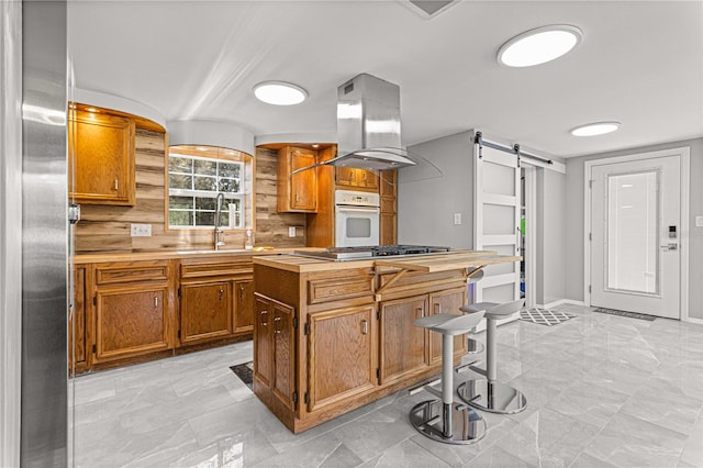 kitchen with a barn door, island exhaust hood, stainless steel appliances, and light tile floors