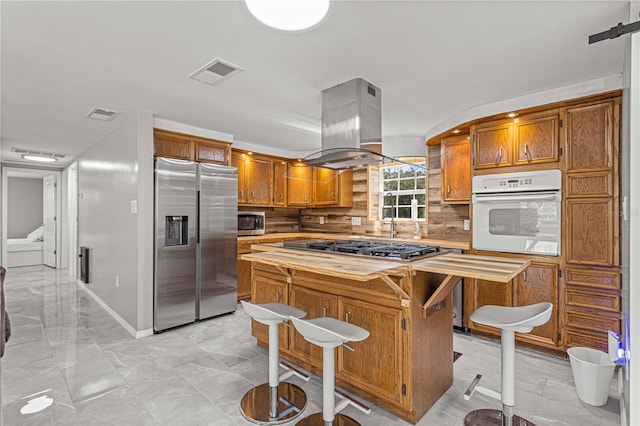 kitchen with backsplash, appliances with stainless steel finishes, light tile floors, a center island, and island range hood