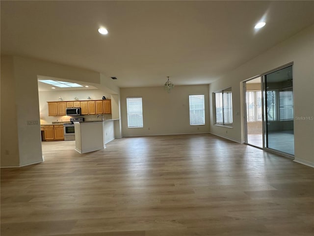 unfurnished living room featuring a chandelier, a wealth of natural light, and light hardwood / wood-style flooring