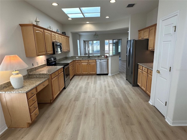 kitchen with dark stone countertops, light wood-type flooring, kitchen peninsula, a skylight, and appliances with stainless steel finishes