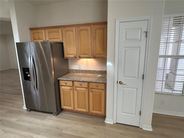 kitchen with light wood-type flooring, stainless steel fridge with ice dispenser, and light stone countertops