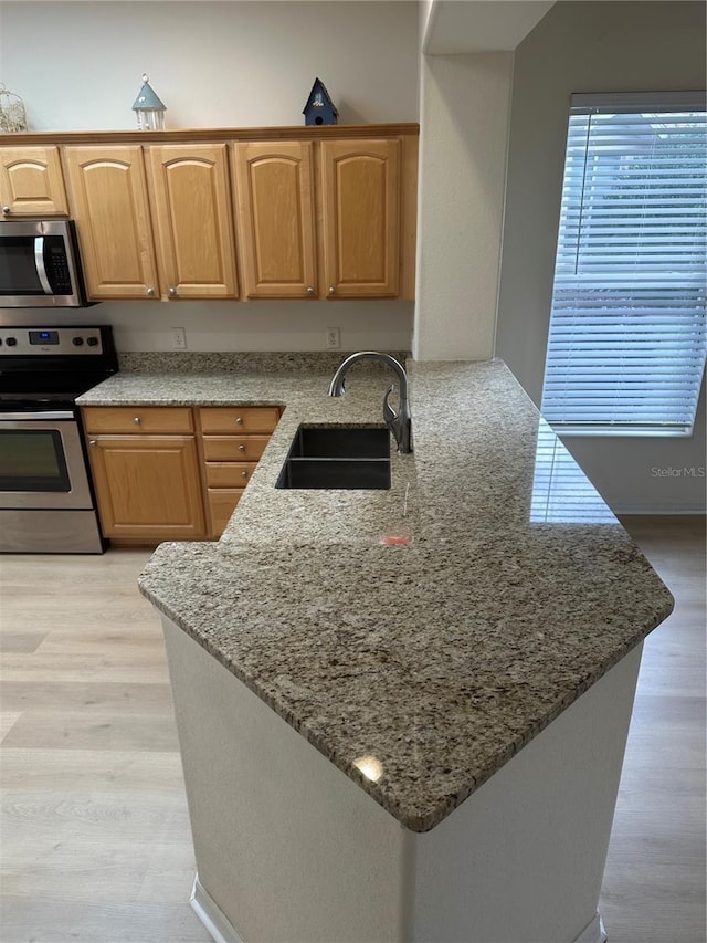 kitchen featuring sink, light stone counters, light hardwood / wood-style flooring, kitchen peninsula, and appliances with stainless steel finishes