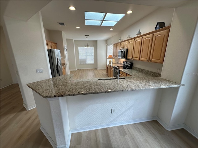 kitchen with stainless steel appliances, a skylight, light stone counters, and kitchen peninsula