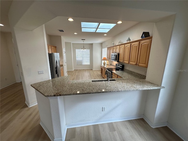 kitchen with light hardwood / wood-style flooring, light stone counters, kitchen peninsula, and appliances with stainless steel finishes