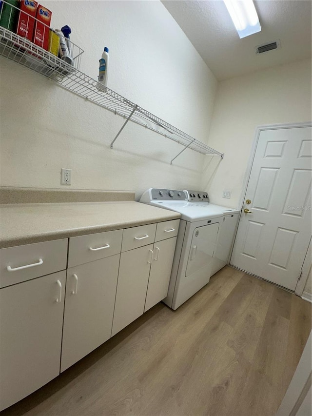 laundry room featuring washer and dryer, light hardwood / wood-style floors, and cabinets