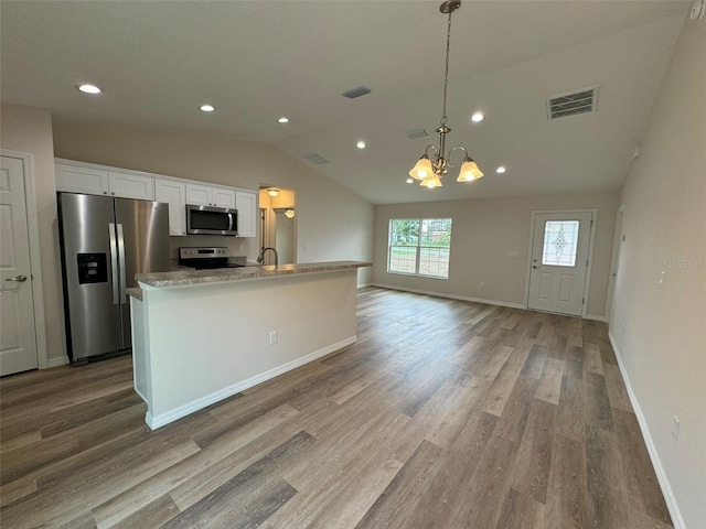 kitchen with lofted ceiling, hanging light fixtures, stainless steel appliances, an island with sink, and white cabinets