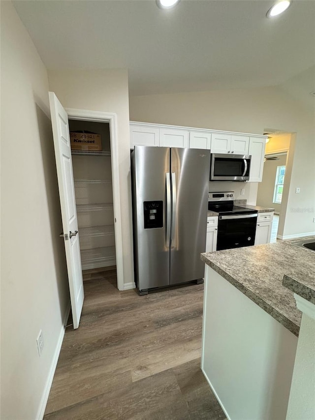 kitchen featuring white cabinetry, light stone counters, vaulted ceiling, appliances with stainless steel finishes, and light hardwood / wood-style floors