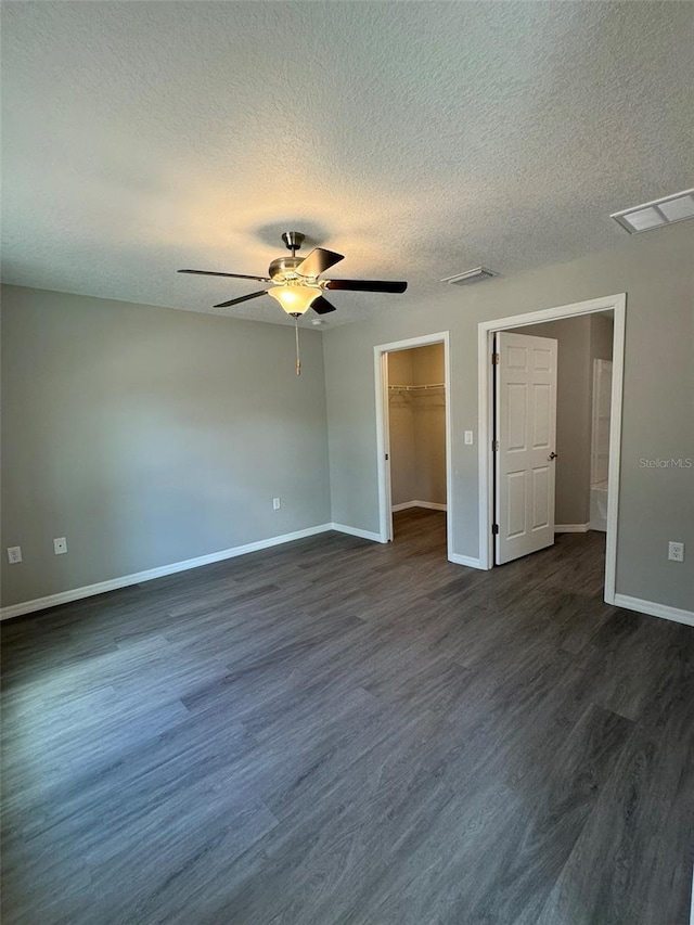 unfurnished bedroom with ceiling fan, a walk in closet, dark wood-type flooring, and a textured ceiling