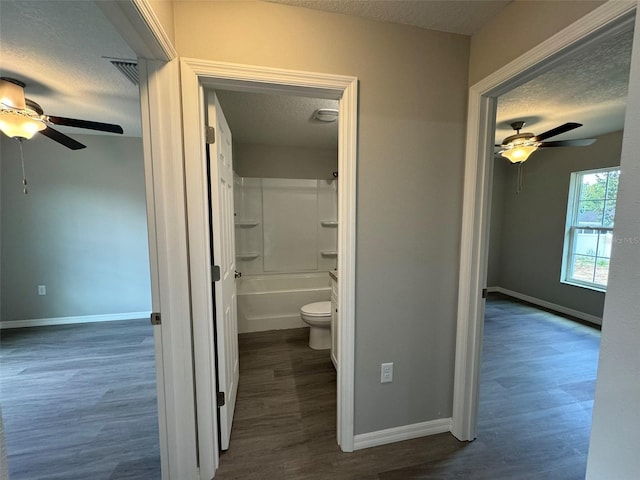 bathroom featuring hardwood / wood-style flooring, shower / tub combination, ceiling fan, a textured ceiling, and toilet