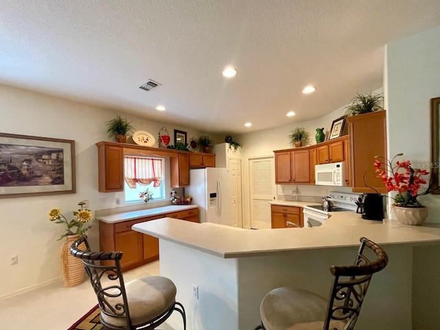 kitchen with a breakfast bar, white appliances, kitchen peninsula, light carpet, and a textured ceiling