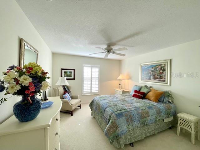 bedroom with ceiling fan, light colored carpet, and a textured ceiling