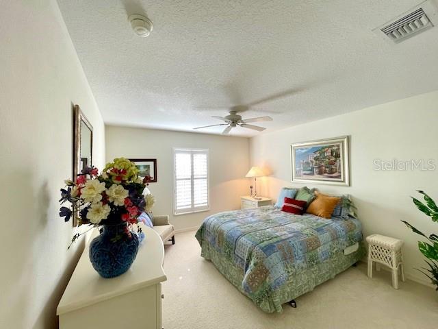 bedroom featuring ceiling fan, light colored carpet, and a textured ceiling