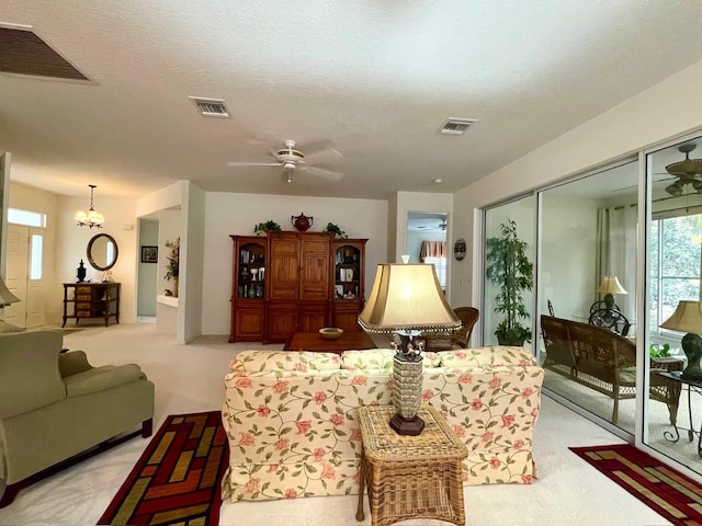 carpeted living room with ceiling fan with notable chandelier and a textured ceiling