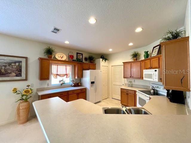 kitchen with sink, a textured ceiling, white appliances, and kitchen peninsula