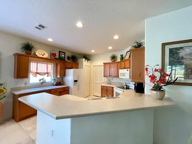 kitchen featuring sink, a textured ceiling, white appliances, and kitchen peninsula