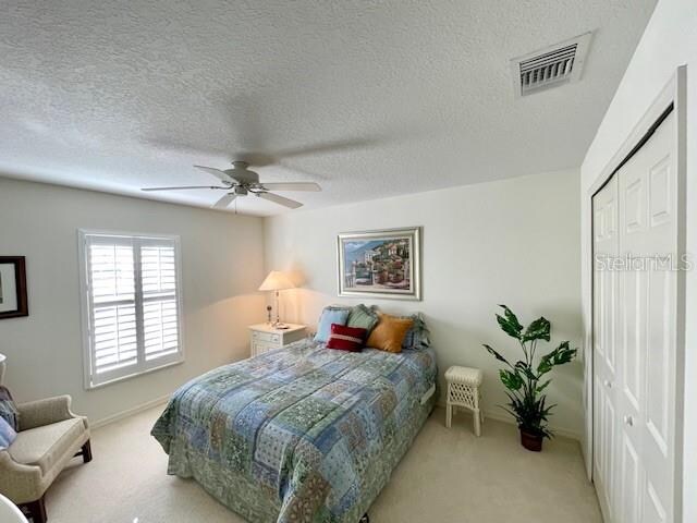 bedroom with a textured ceiling, light colored carpet, a closet, and ceiling fan