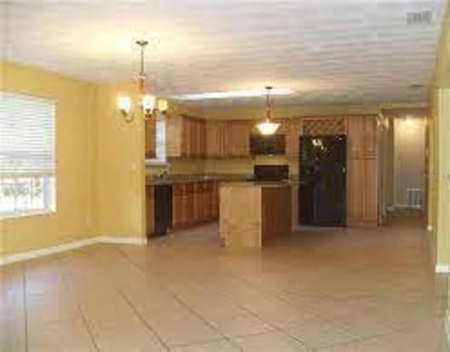 kitchen featuring a notable chandelier, decorative light fixtures, black fridge, and a center island