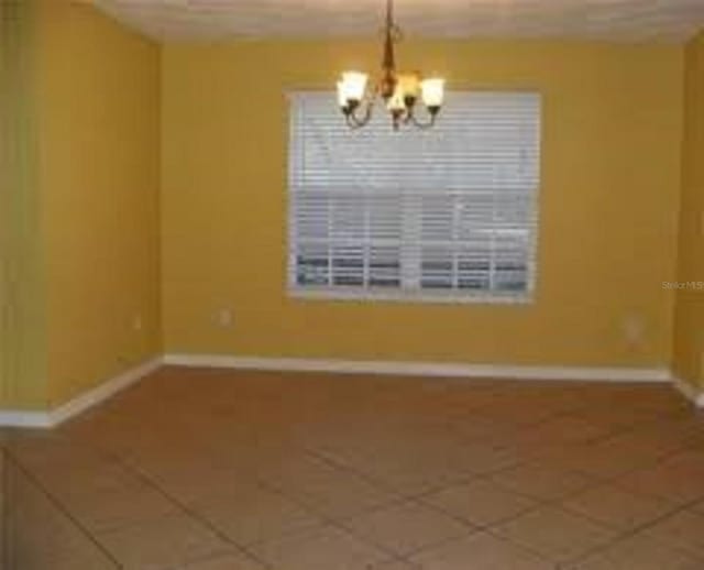 tiled empty room with an inviting chandelier