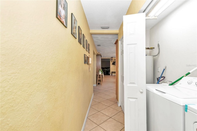 corridor with light tile flooring, separate washer and dryer, and a textured ceiling